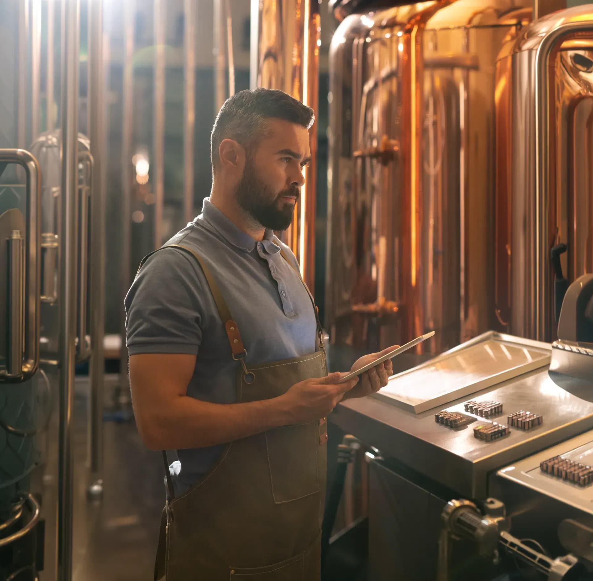 Cellar worker checking a tablet beside copper fermentation tanks