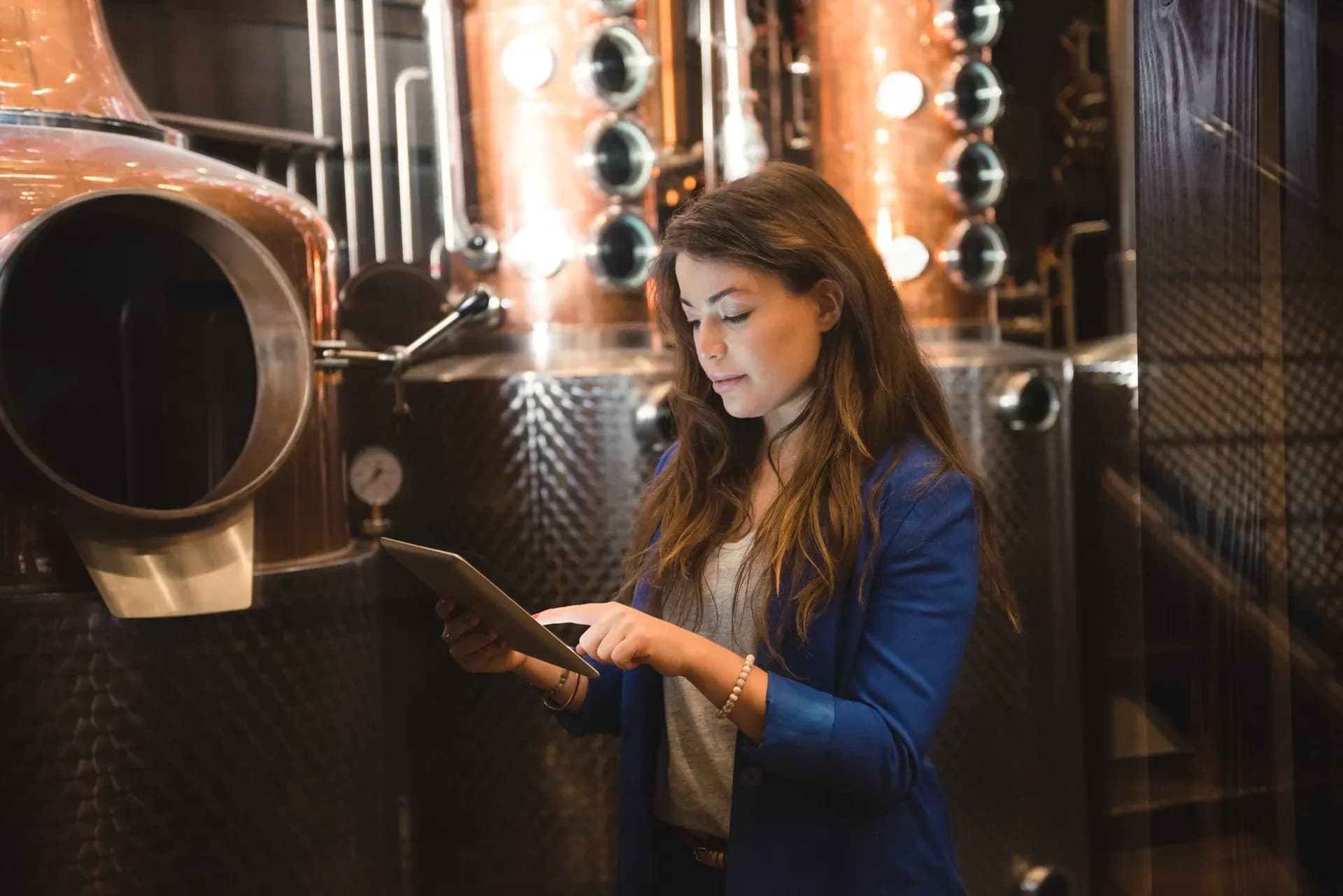 Wine merchant using a tablet in front of copper stills and steel tanks